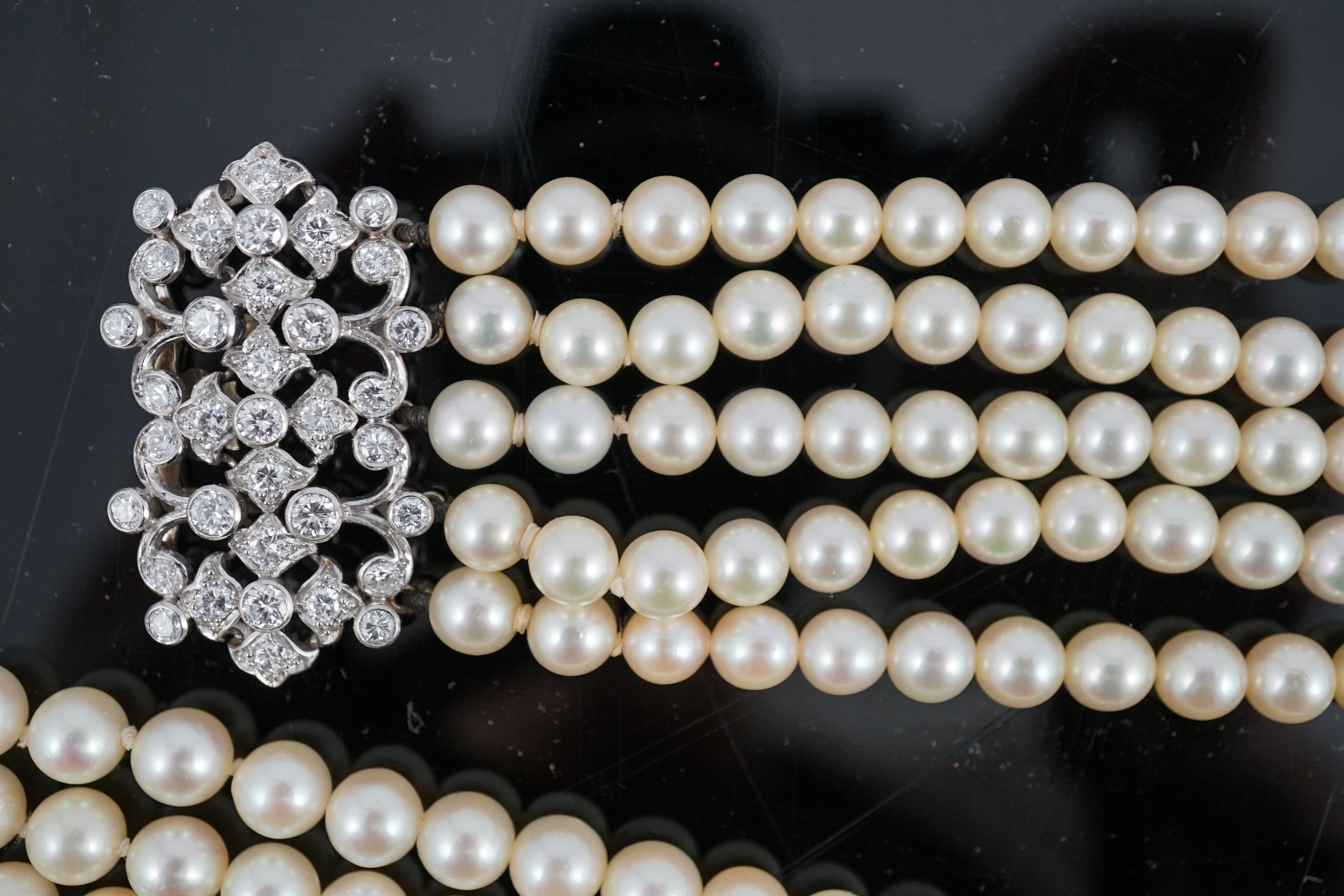 A mid 20th century quintuple strand cultured pearl choker necklace, with diamond cluster set white gold clasp and diamond cluster set white gold scrolling central motif, together with a matching bracelet